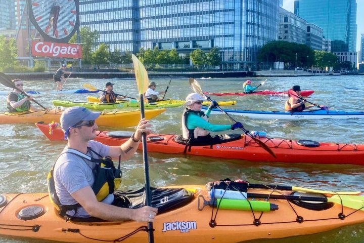 a group of people riding kayaks in the water with the Colgate Clock in the background