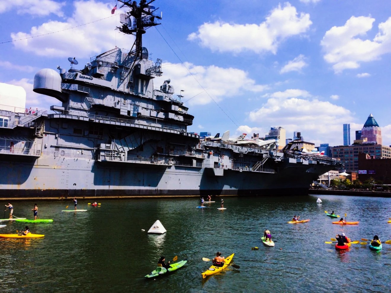 a large ship in a body of water with USS Intrepid Museum in the background