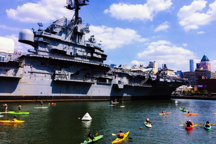 a large ship in a body of water with USS Intrepid Museum in the background