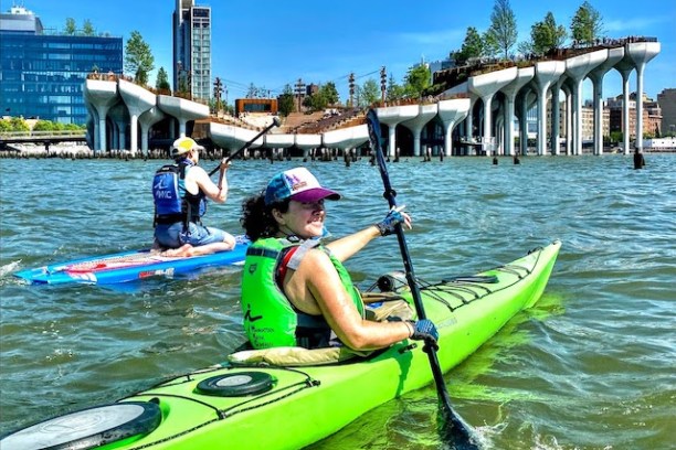 a woman in green sea kayak and man on a stand up paddle board in front of Little Island on the Hudson River in NYC