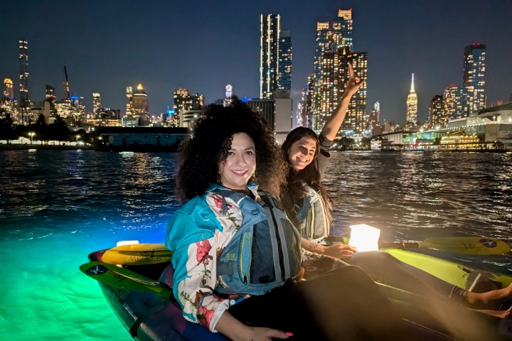 Two woman kayaking at night on the Hudson River in NYC with city lights