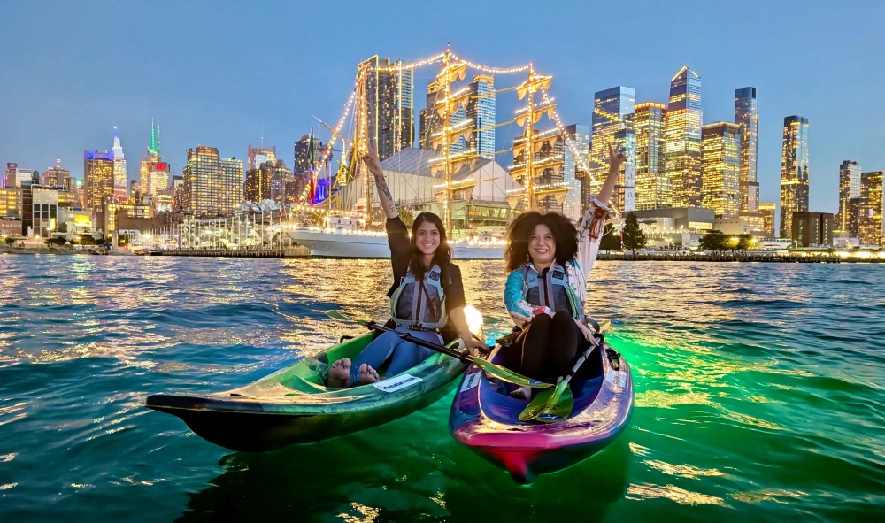 Two woman kayaking at night on the Hudson River in NYC with the Mexican Navy ship in the background