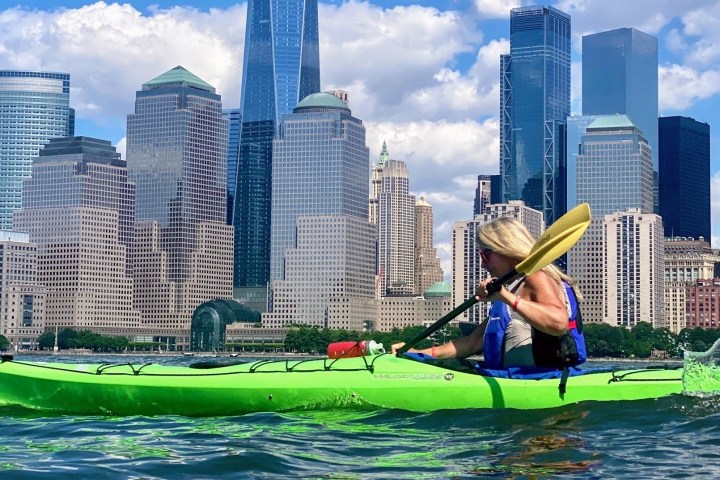 a woman riding a green kayak in front of the Freedom Tower