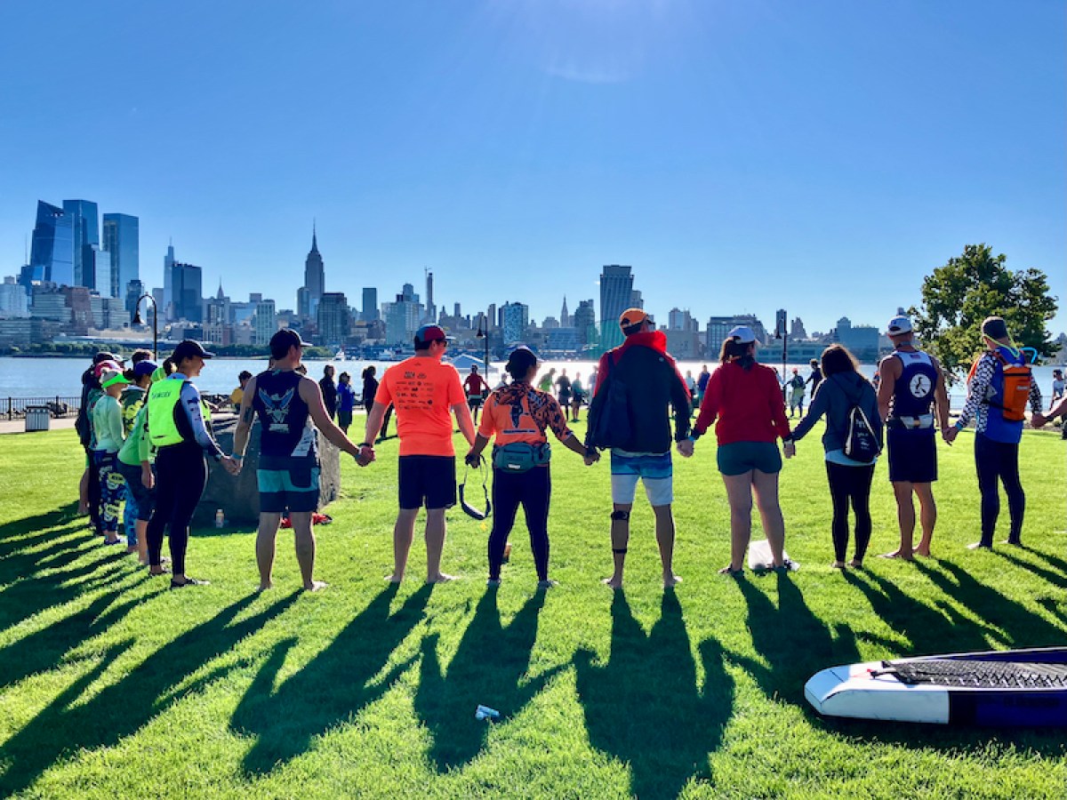 Manhattan Kayak members join a larger group of racers in a circle, holding hands, at the Hudson River Cup race in Hoboken..