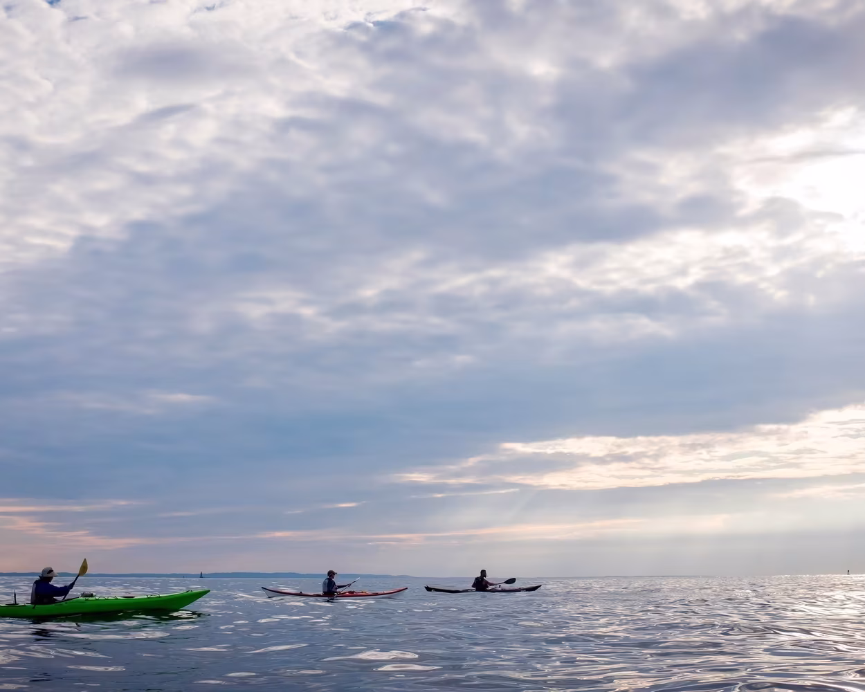 Five kayakers at the center of infinite skies and open water. Undulating reflections of light surround them. There is a steady rhythm shared by their breath, their strokes, and rippling water. The sun, shrouded by clouds, inches slowly toward the western horizon as they paddle toward it from Coney Island Beach to the Verrazzano Narrows. These kayakers are on the way home from Manhattan Kayak Co's 33-mile single-day Coney Island Trip.