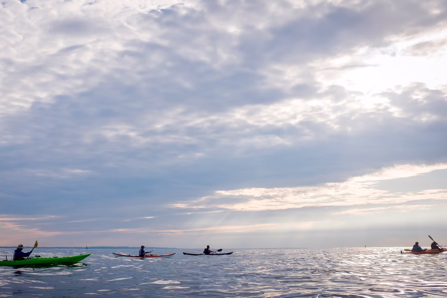 Five kayakers at the center of infinite skies and open water. Undulating reflections of light surround them. There is a steady rhythm shared by their breath, their strokes, and rippling water. The sun, shrouded by clouds, inches slowly toward the western horizon as they paddle toward it from Coney Island Beach to the Verrazzano Narrows. These kayakers are on the way home from Manhattan Kayak Co's 33-mile single-day Coney Island Trip.