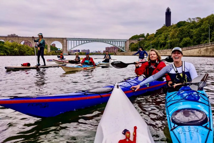 Group kayaking and paddleboarding on the Harlem River with the Washington Bridge in the background..
