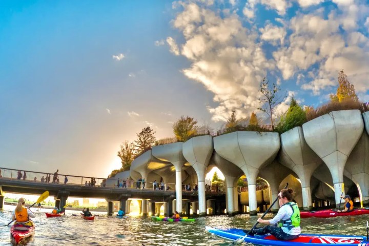 People kayaking and paddleboarding near a pedestrian bridge with the unique tulip-shaped concrete supports of Little Island at sunset during the West Village Trip.