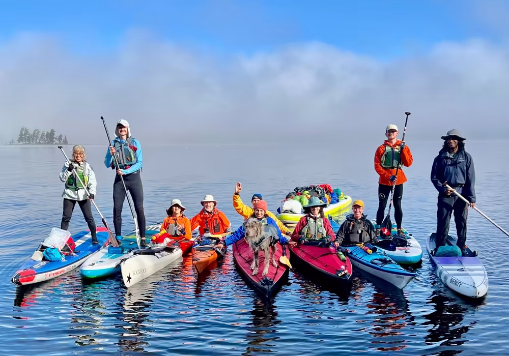 A diverse group of Manhattan Kayak Co Adventure Club members on paddleboards and kayaks with a dog during a misty morning session on the water.