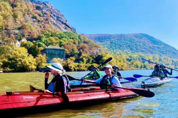 A joyful group of six Manhattan Kayak Co members paddle tandem sea kayaks past the Breakneck Tunnel, enjoying the peak fall foliage of the Hudson Highlands during an exclusive members-only day trip.