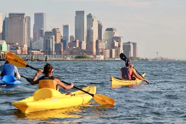 Kayaking the NYC skyline with professional guides on the Hudson: A Manhattan Kayak Co kayak guide leads two beginners in stable sit-on-top kayaks toward the downtown NYC skyline, demonstrating the safe and relaxed pace of guided river trips.