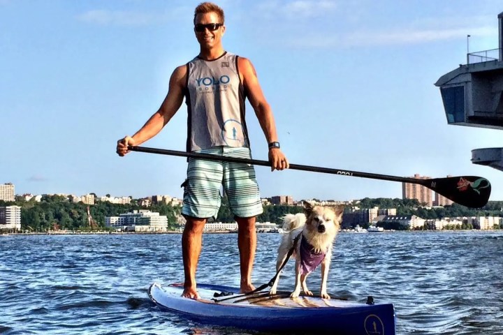 A man enjoying a 45-minute easy paddleboarding session at Pier 84 with his dog—no experience needed and double the time of free programs.