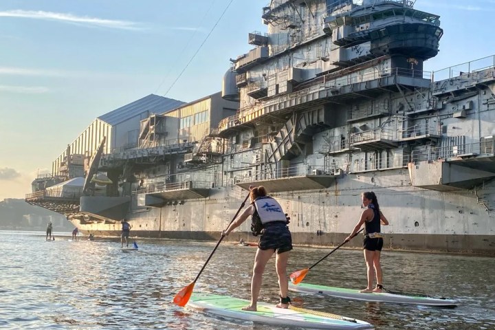 Two women renting paddleboards and practicing their stroke technique along the USS Intrepid during the public rental program.