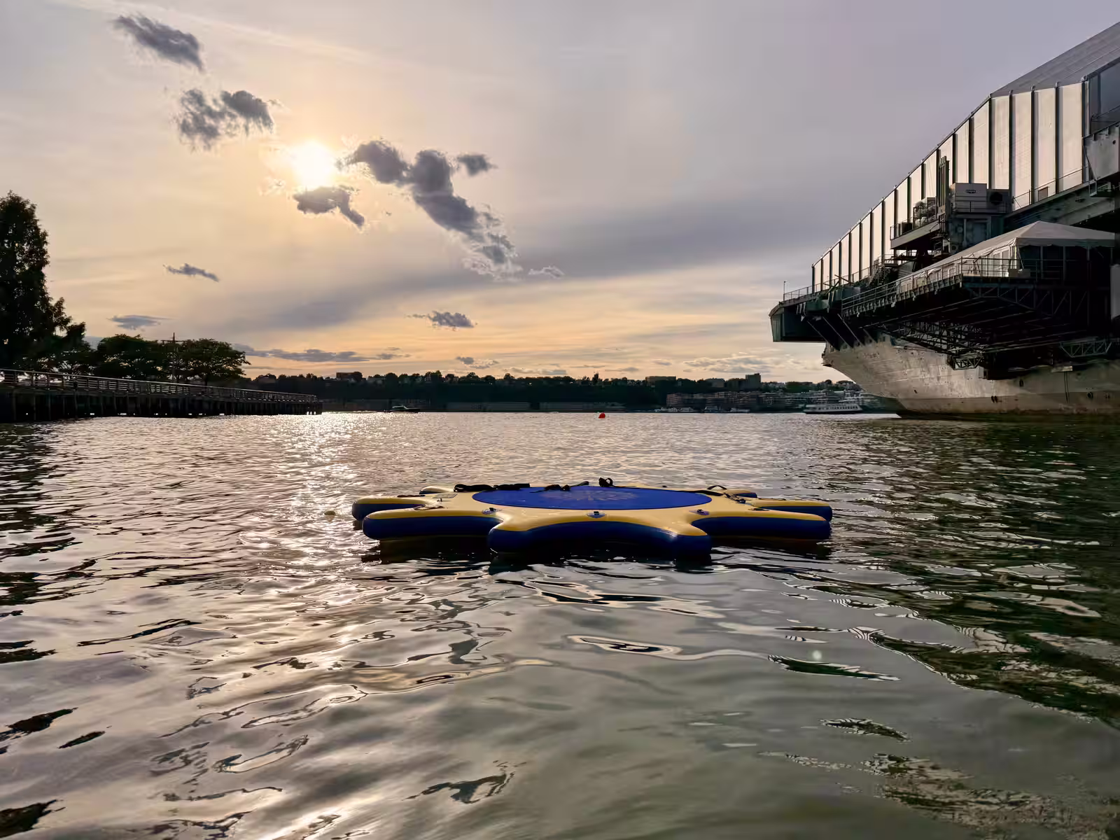 Floating platform shaped like a star on a river near the Intrepid at sunset.