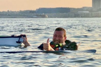 A man in the Hudson River holding onto a sea kayak