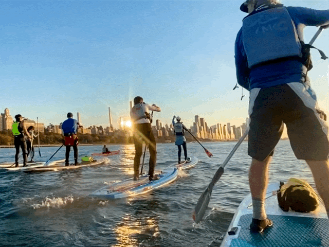 Group paddleboarding towards a city skyline at sunset on the Hudson River.