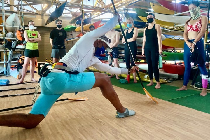 A man teaching a class on stand up paddle boarding to a group of people inside the Pier 84 boathouse