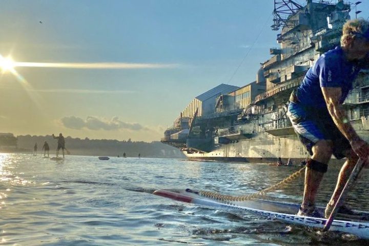 An expert paddleboarder riding along the Intrepid Museum.