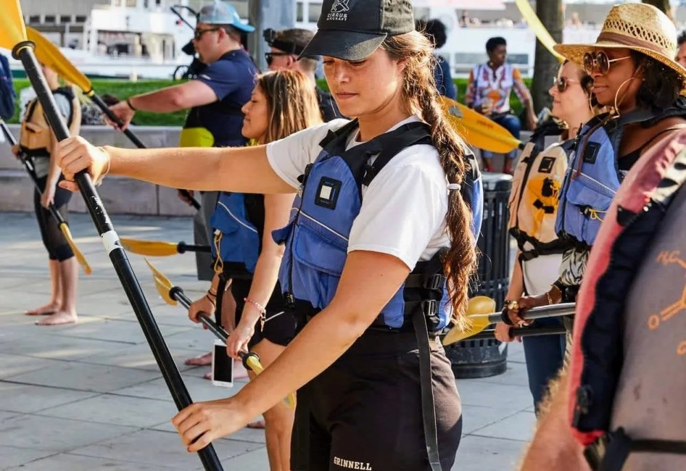 Beginners receiving a professional kayak lesson and safety briefing on a paved waterfront park at a Manhattan boathouse before their private river trip.