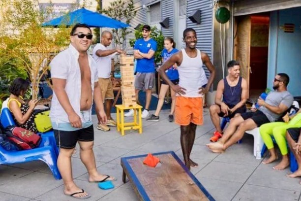 Guests playing cornhole and giant Jenga on a sunlit patio at the Manhattan Kayak boathouse.