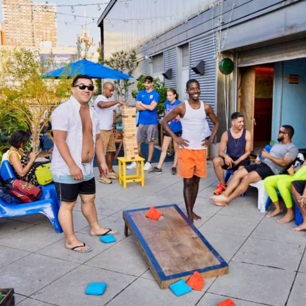 Guests playing cornhole and giant Jenga on a sunlit patio at the Manhattan Kayak boathouse.