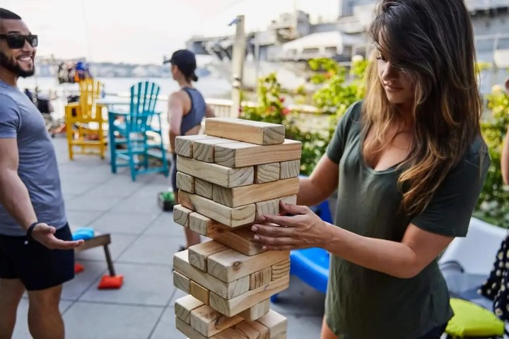 Young professionals playing giant Jenga and lawn games on a private waterfront patio during a corporate summer outing at a Hudson River boathouse.