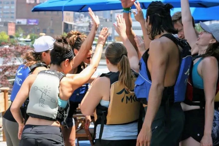 A cheering corporate team celebrating with high-fives on a waterfront patio after a successful NYC private kayak trip.