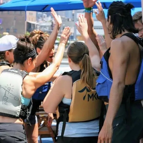A cheering corporate team celebrating with high-fives on a waterfront patio after a successful NYC private kayak trip.