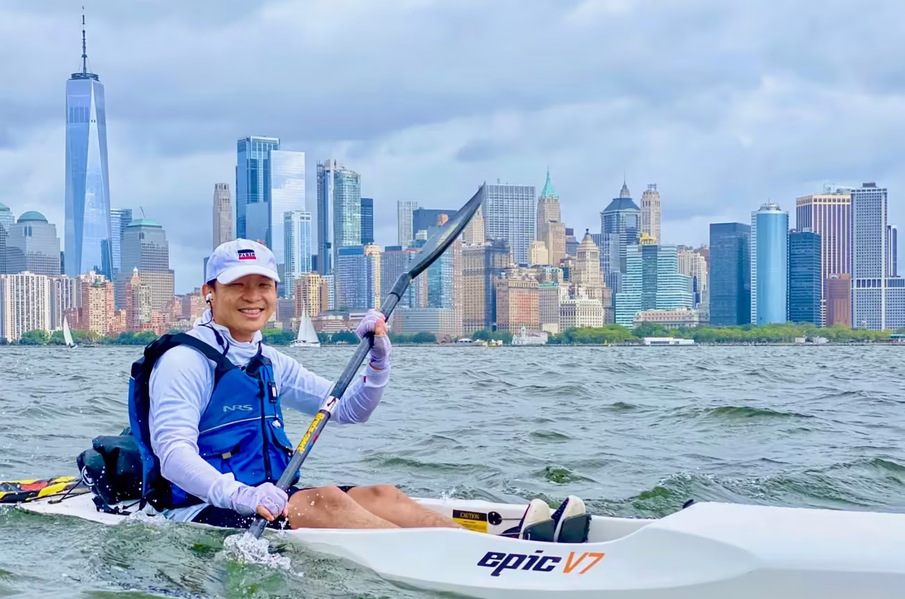 A man riding an Epic V7 surfski in front of the downtown Manhattan skyline with the Freedom Tower in the background.