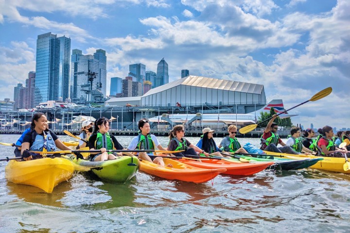 a student group kayaking in front of Times Square, Hudson Yards, and the Intrepid Aircraft Carrier