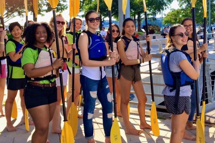 a private group of female students waiting in line with kayak paddles