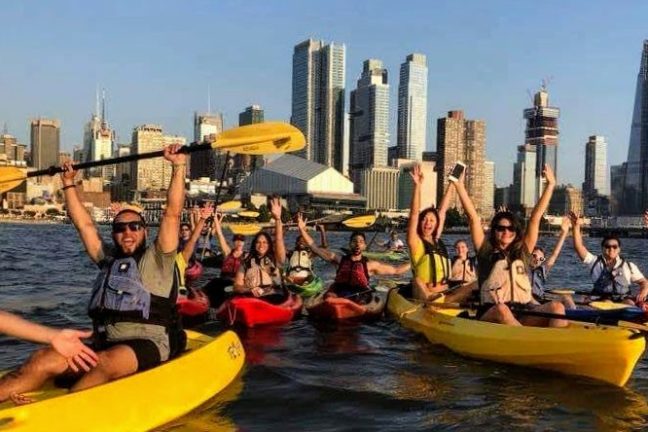 a group raising their paddles and shouting while kayaking things to do in NYC with a group