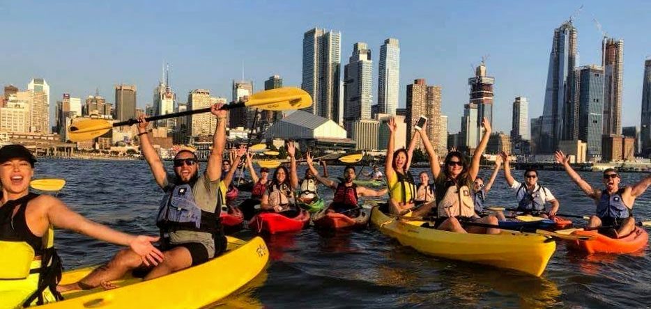 a group raising their paddles and shouting while kayaking things to do in NYC with a group