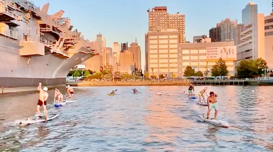 A group of paddleboarders in the cove at Pier 84 riding in two straight lines during Manhattan Kayak Co's Speed Training.
