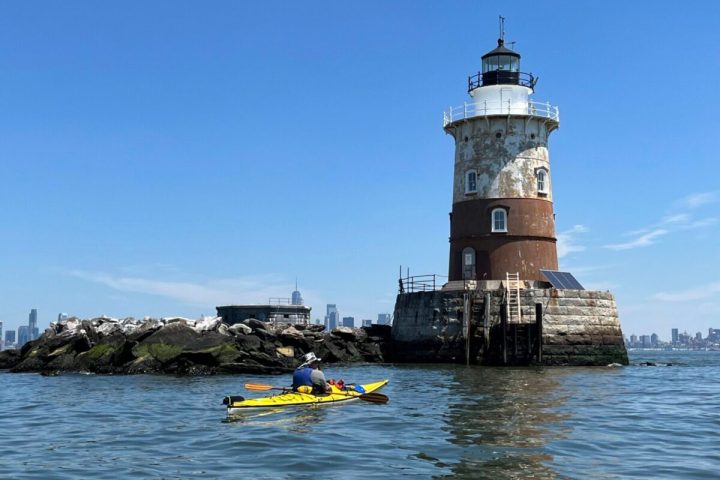 a man riding in a yellow kayak in front of the Robbins Reef Lighthouse