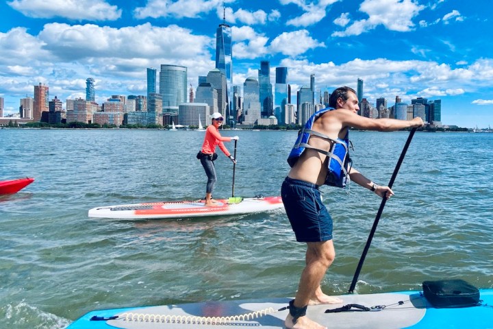 a man and a woman riding stand up paddle boards on the Hudson River in NYC