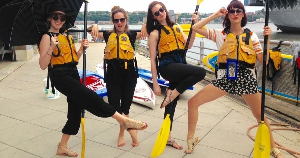 What To Wear For Kayaking four women posing wearing life jackets and holding kayak paddles