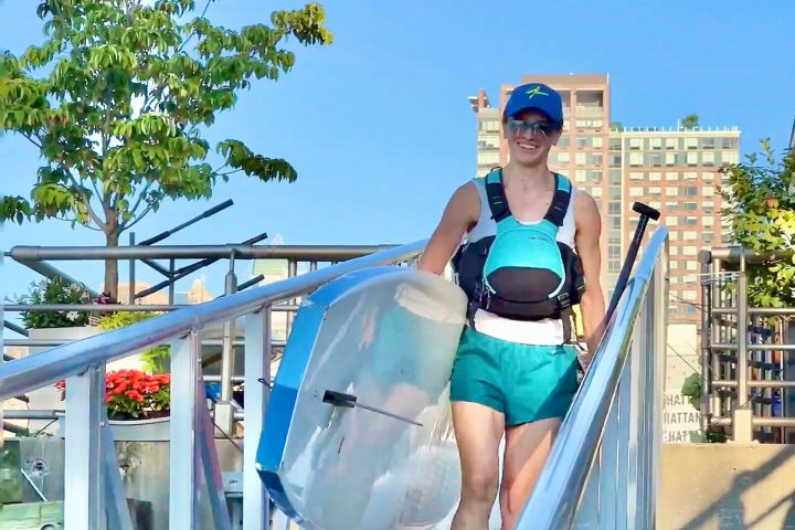 a woman carrying a stand up paddle board down a ramp
