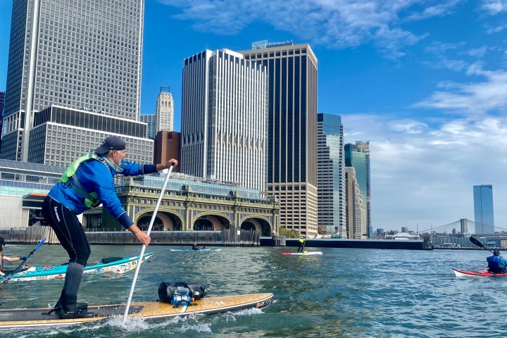 a man paddle boarding on a body of water in front of Battery Maritime Building