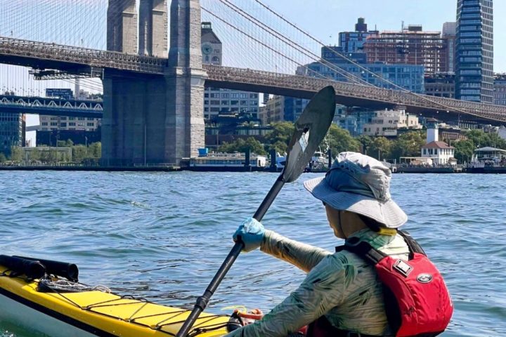 a man riding on a kayak in front of the Brooklyn Bridge