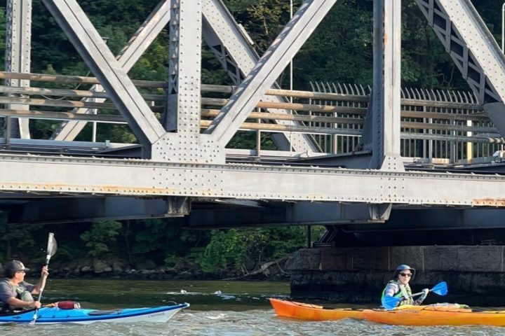 Two kayakers paddling under the Henry Hudson Bridge.