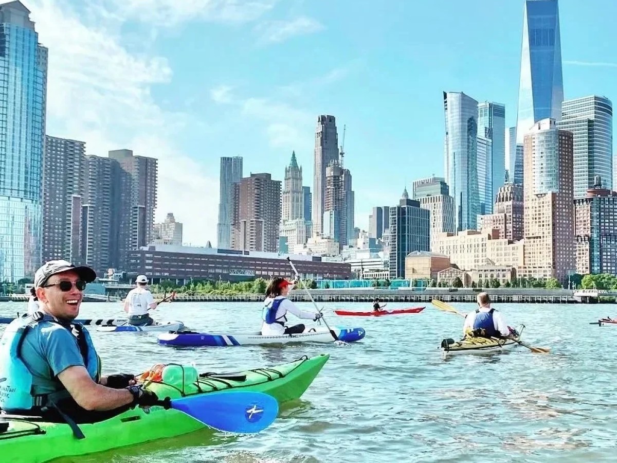 A group of Manhattan Kayak Co members in colorful sea kayaks paddle through a light swell toward One World Trade Center at the start of a 30-mile circumnavigation trip.