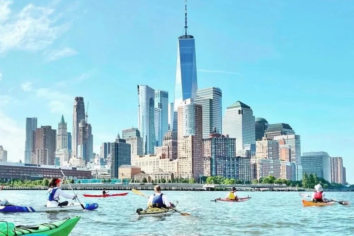 A group of Manhattan Kayak Co members in colorful sea kayaks paddle through a light swell toward One World Trade Center at the start of a 30-mile circumnavigation trip.
