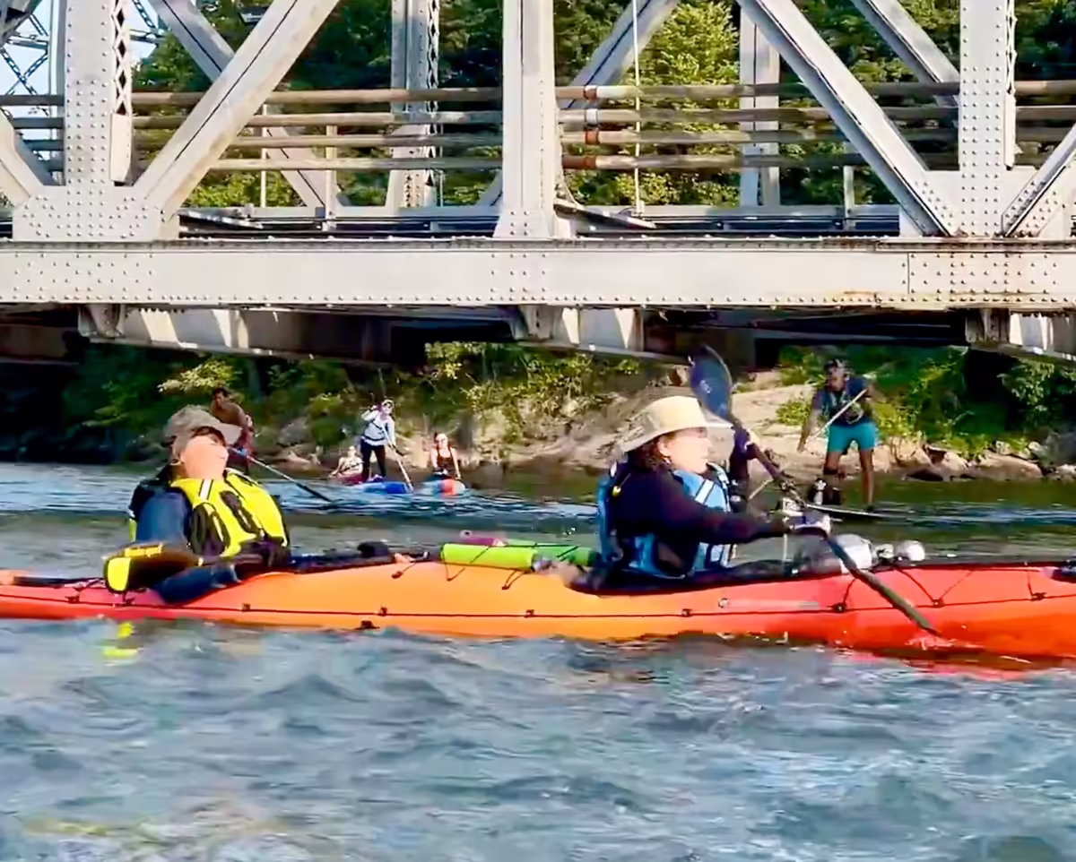 A couple riding a tandem sea kayak at the Spuyten Duyvil Bridge.