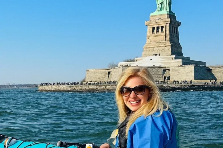 A woman kayaking in front of the Statue of Liberty with Manhattan Kayak Co.