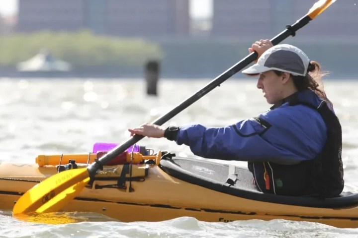 A focused student at Manhattan Kayak Co demonstrates a perfect high-angle stroke on the Hudson River, showing upright posture, a wide paddle grip, and correct forward gaze during a Kayak Basics class.