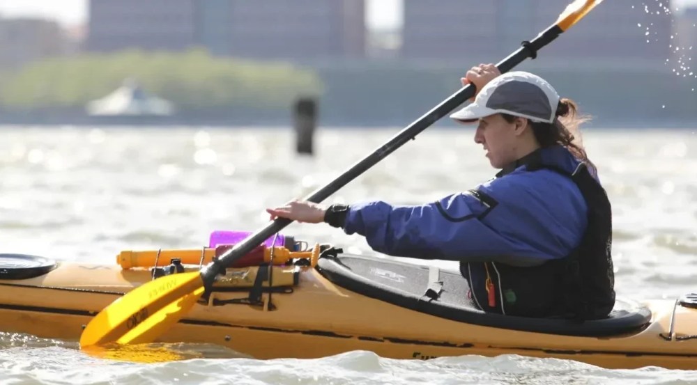 Woman learning how to sea kayaking in a beginner class on the Hudson River, paddling a sit-inside sea kayak near Manhattan Kayak Co