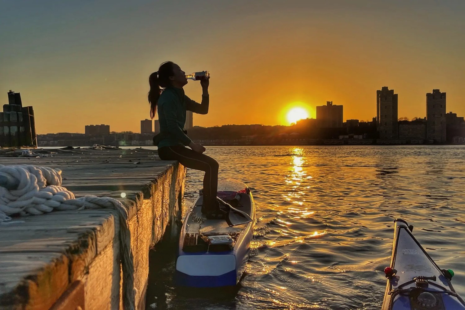 Paddleboarder drinking water along the Hudson River at sunset