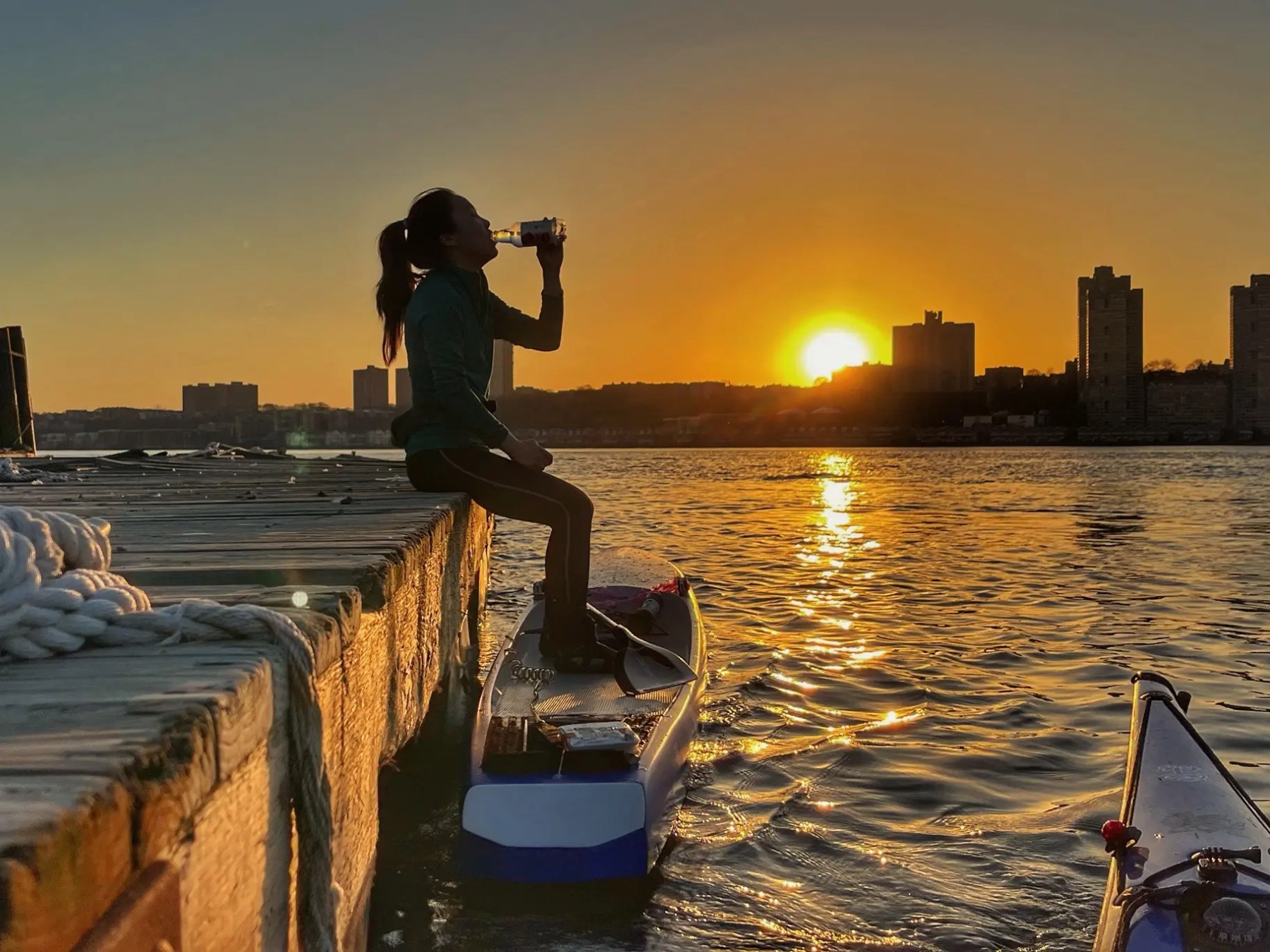 Paddleboarder drinking water along the Hudson River at sunset