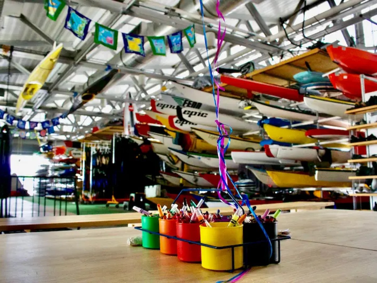 Colorful markers in cups on a table in a kayak storage area with boats and flags.